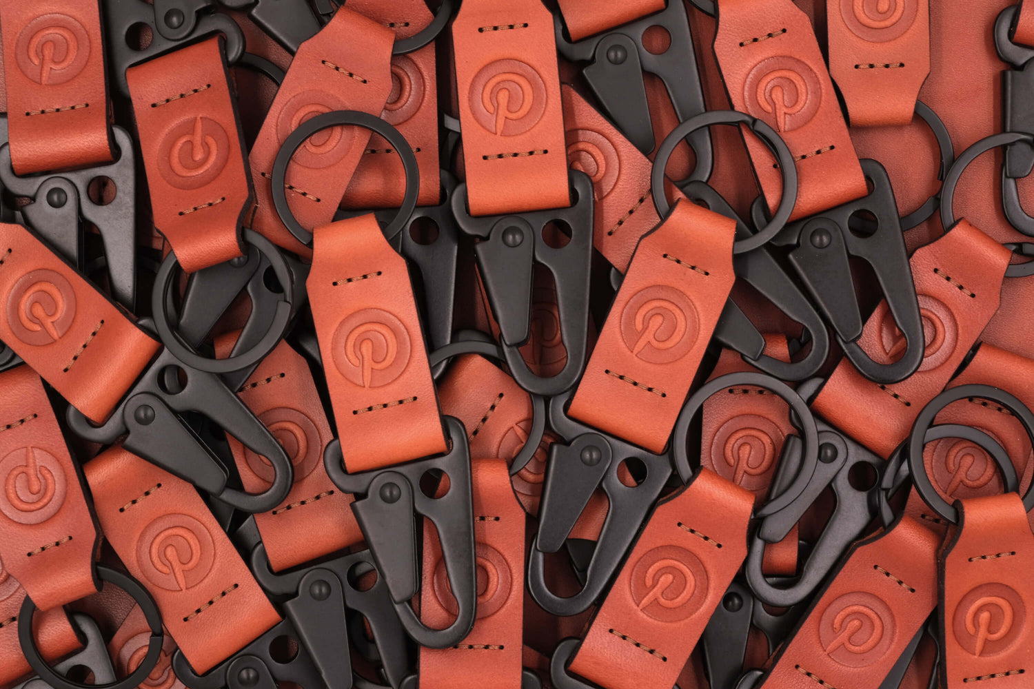 Pile of brown leather Clip Keychains with Pinterest logo and black hardware.