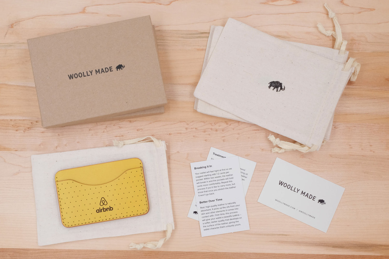 Sustainable brown box, canvas drawstring bags, and business cards with Woolly Made logo and a yellow leather Slim Wallet with decorative perforation and Airbnb logo.