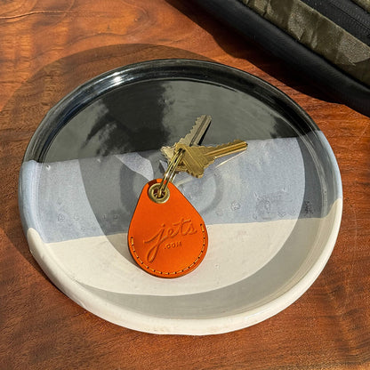 Orange leather AitTag Keychain Jets.com Embossed detail. The keychain is on a plate in a bright sunny photo on a wooden table
