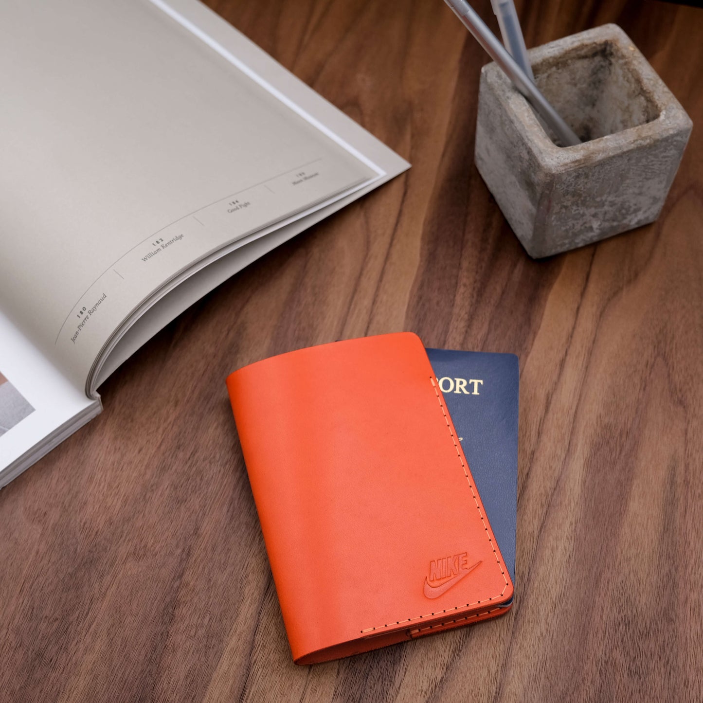 Woolly Made Passport Cover debossed for promotional gifting. On a dark wood table and a concrete pen holder.