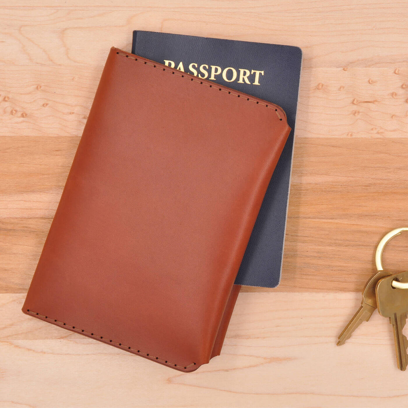 Brown leather passport wallet closed view with passport and keys on a desk.