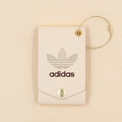 Tusk leather leather luggage tag with fold closure, brass hardware, and Adidas logo.