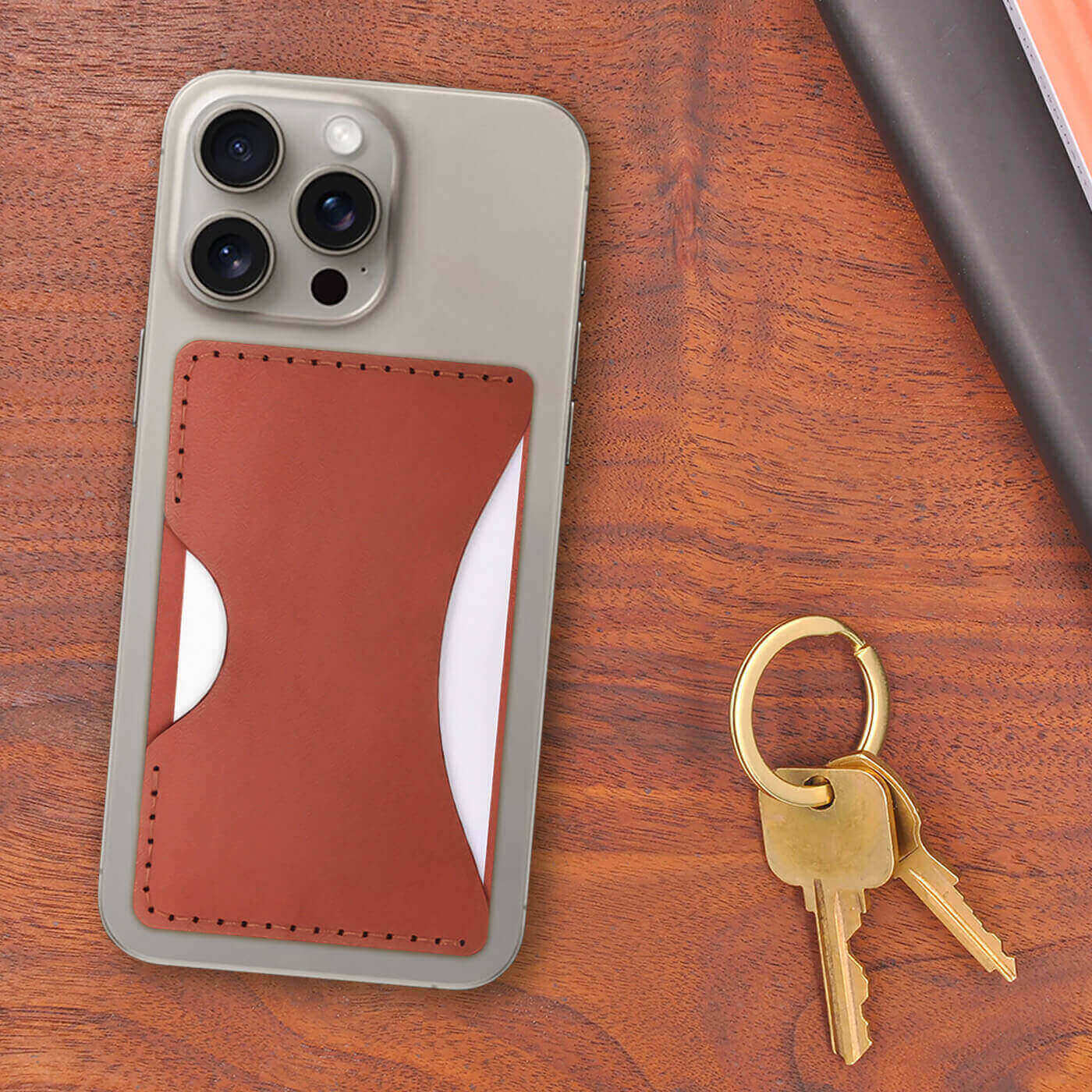 Brown leather Stick-On Wallet with white cards on iPhone next to a set of books and keys.