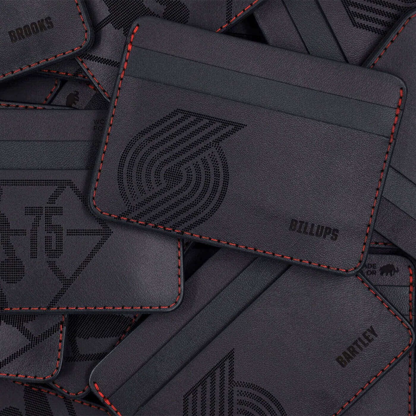 Pile of black leather half wallets with red stitching, Portland Trail Blazers logo and custom etched names.