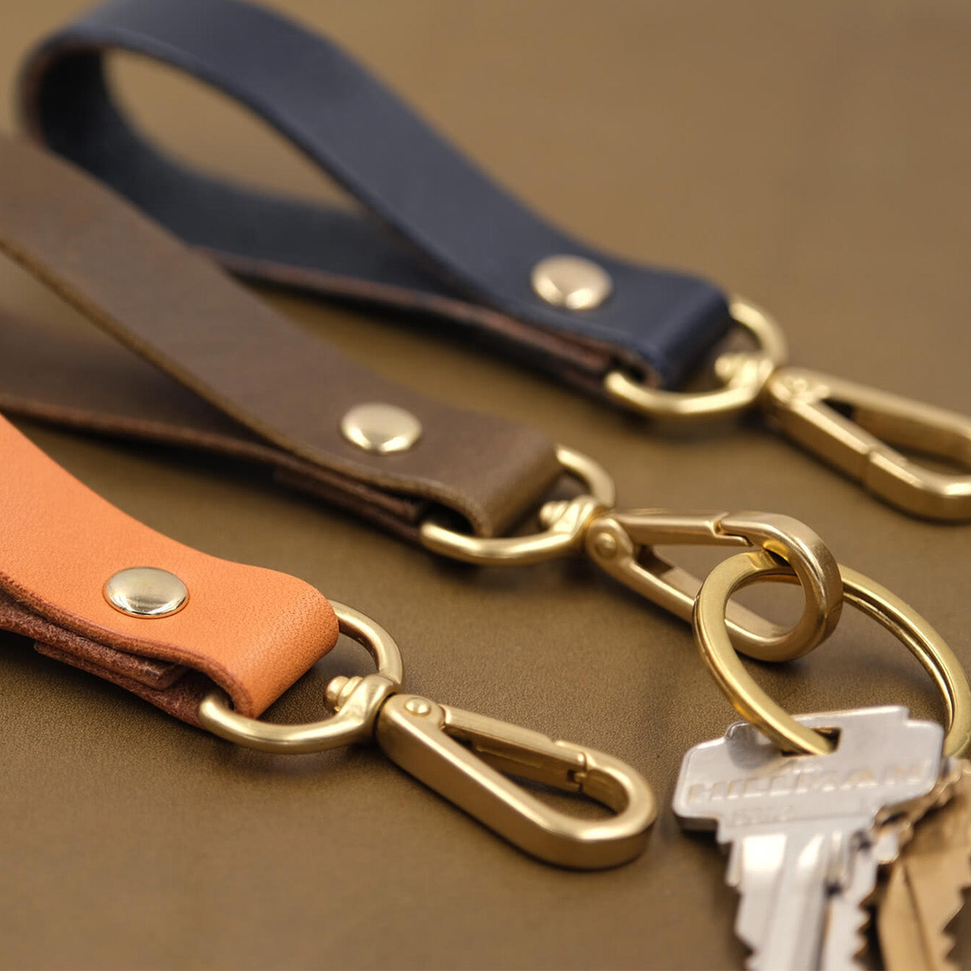 Navy, olive, and tan Loop keychains with brass hardware and keys